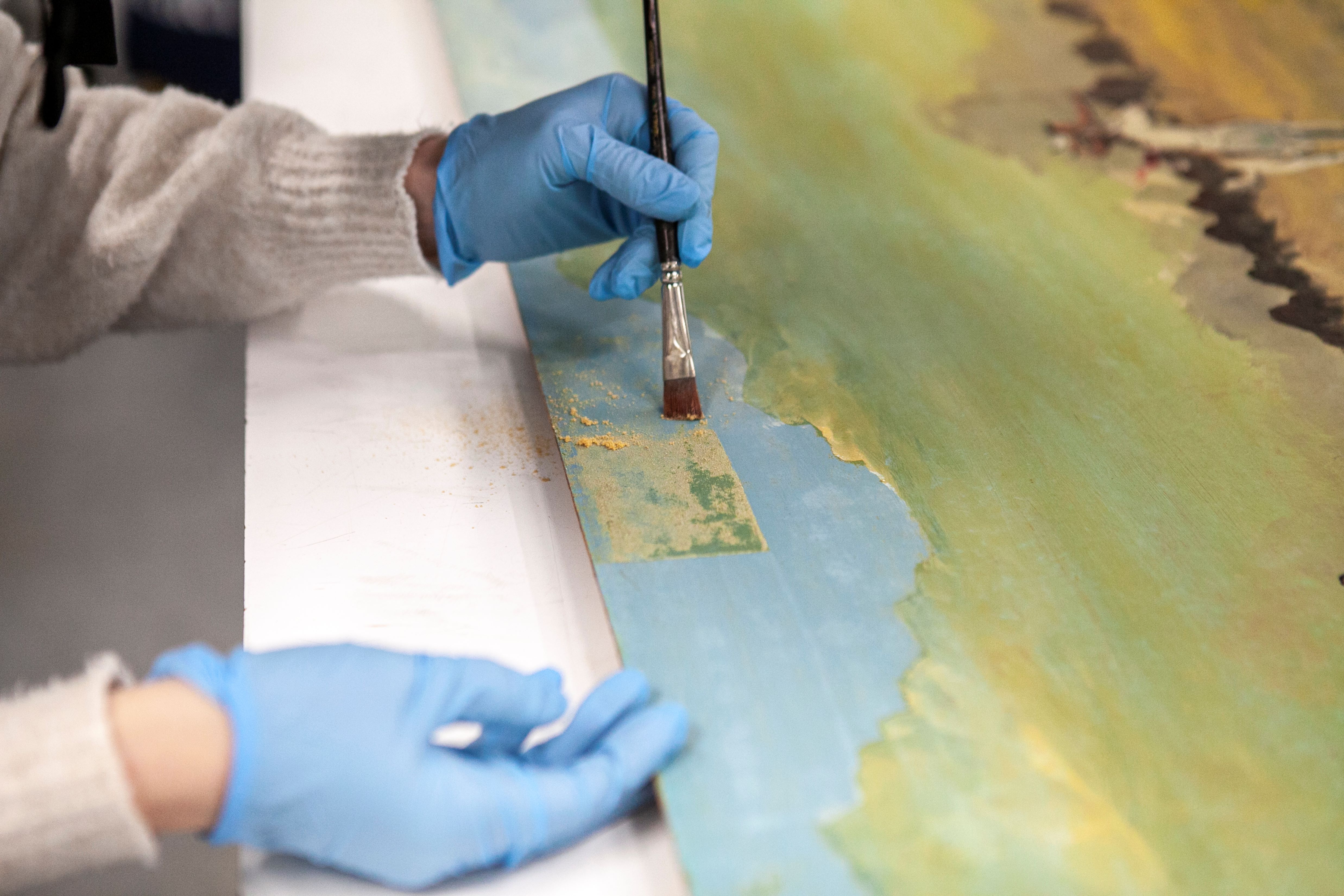 Beaudry, H - The Buffalo Hunt, SK Arts Permanent Collection – Closeup shot of a young woman, C Foster brushing desiccated varnish from a sky.