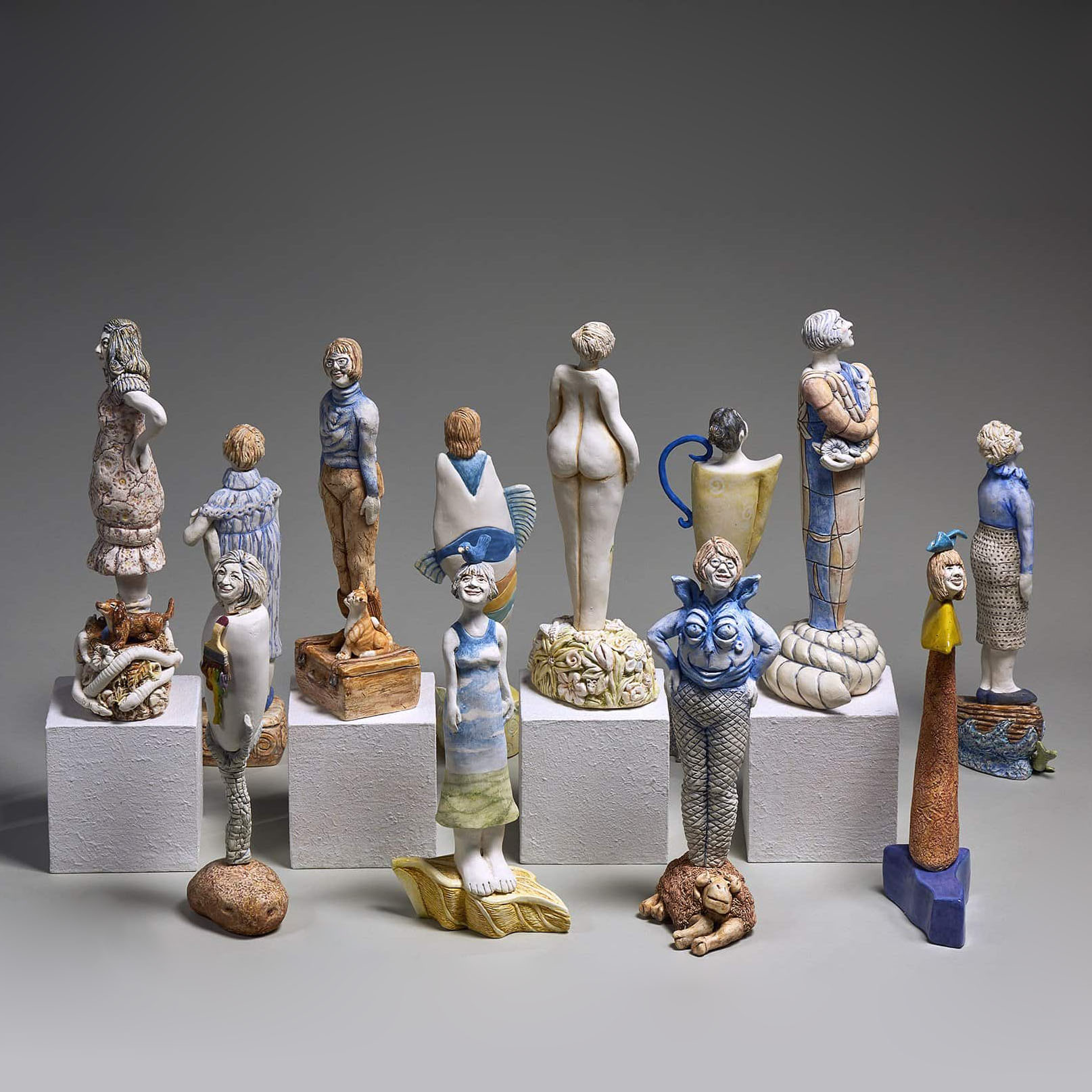 SK Arts Permenent Collection Piece, Art Rental Saskatchewan: Deborah Potter sculpture: 40+ Years in the Making. Product picture of 12 piece  scilpture of miniature women ceramicists in Saskatchewan. the picture has a gret background. The scuplture features Karen Dahl, Maria Gakovic, Beth Hone, Ann James, Margaret Keelan, Marilyn Levine, Sandra M. Ledingham, Jeannie Mah, Lorraine Malach, Anne McLellan, Wendy Parsons, Deborah Potter, and Anita Rocamora.