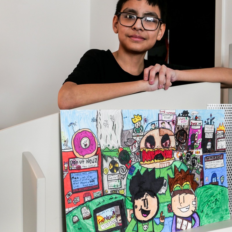 Caine Head – Young boy wearing glasses and a black shirt with his artwork.