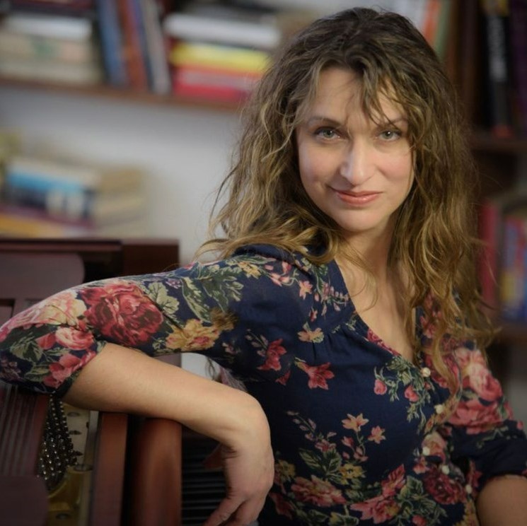 Dara Schindelka - Woman with curly hair and wearing floral dress