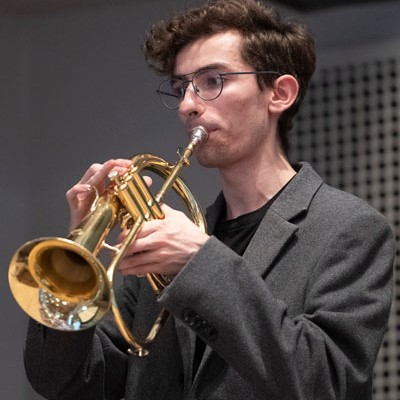 Graeme Dyck - Young man wearing glasses and a gray jacket blowing a saxophone