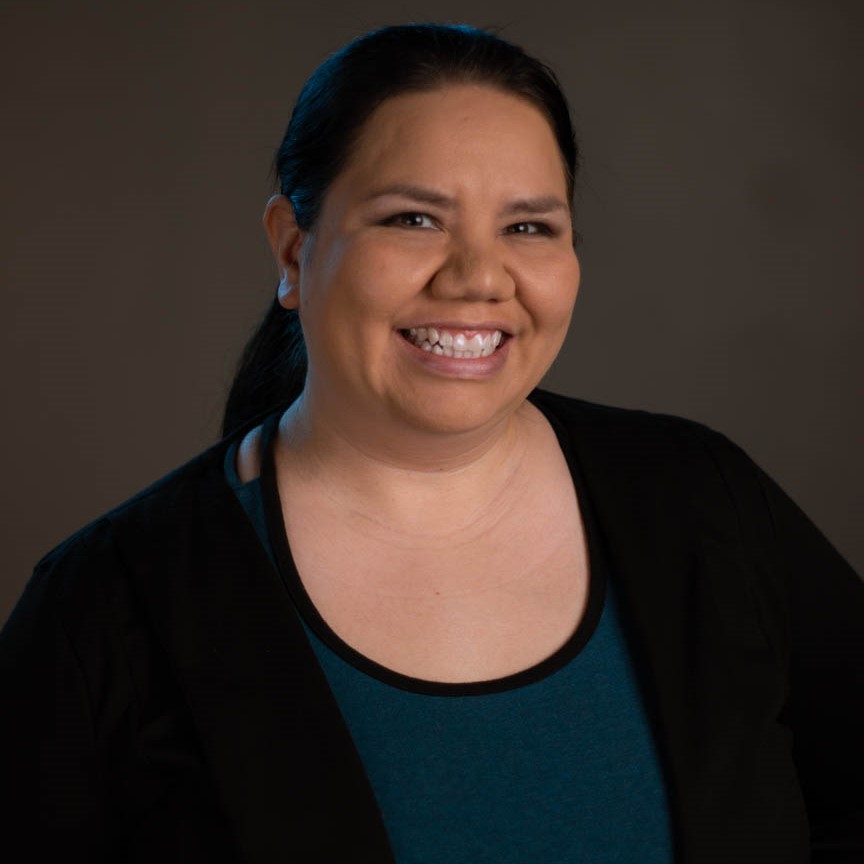 Jennifer Dawn Bishop - Portrait of Indigenous woman smiling, She is wearing s black cardigan and blue blouse.