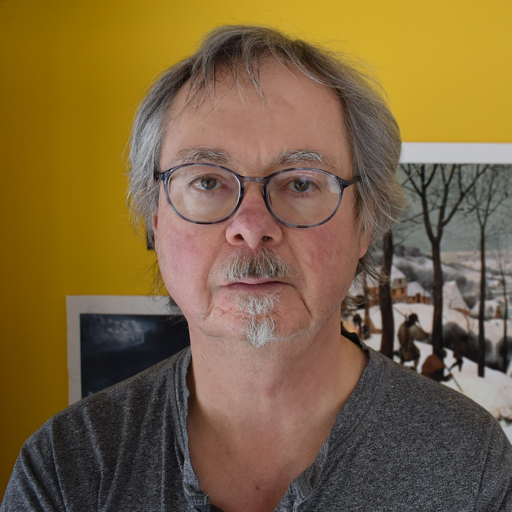 Michael Trussler - Older man with grey hair, eyebrows and mustache. He is wearing glasses and a grey t-shirt.