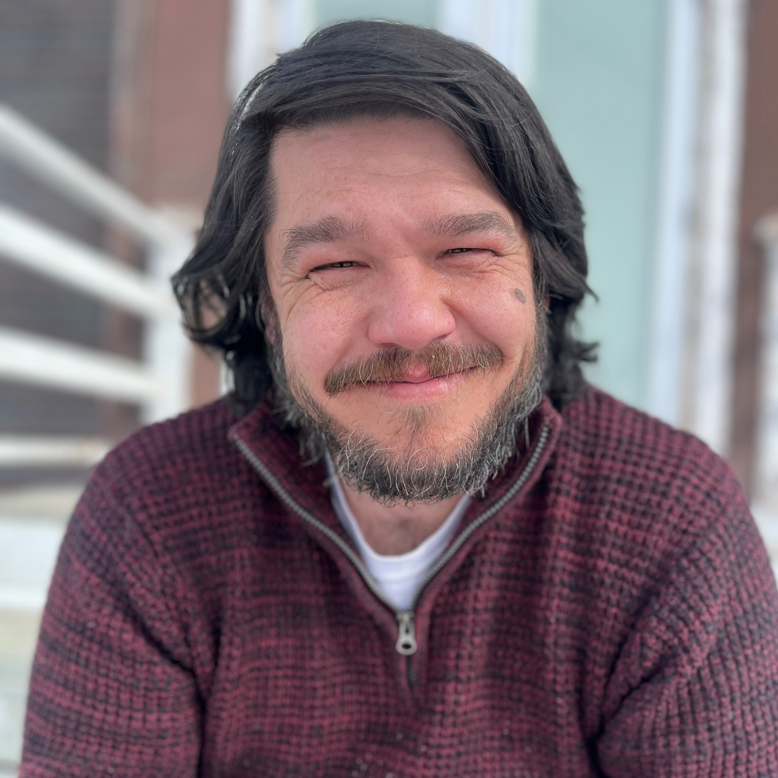 Tim Blackett - Portrait of smiling man with dark hair wearing a burgundy knitted sweater.