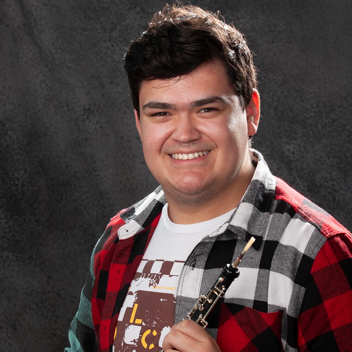 Tyrell Hardlotte - Portrait of young man smiling wearing red, white and black plaid, holing obo.