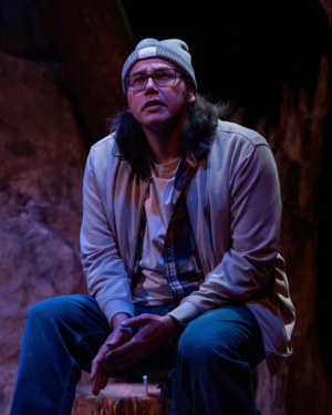 Portrait of Indigenous an wearing a grey beanie, and jacket, blue jeans sitting under a blue light and looking up - Danny Knight