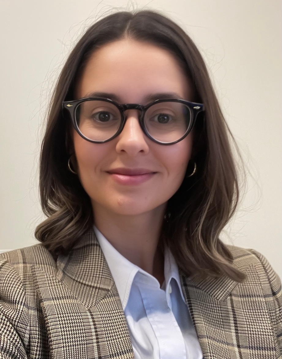 Andrea Muholland, Management Consultant SK Arts Board Mmember - Portrait of woman with long brown hair and large rimmed black glasses. She is wearing a khaki coloured checkered blazer and white undershirt