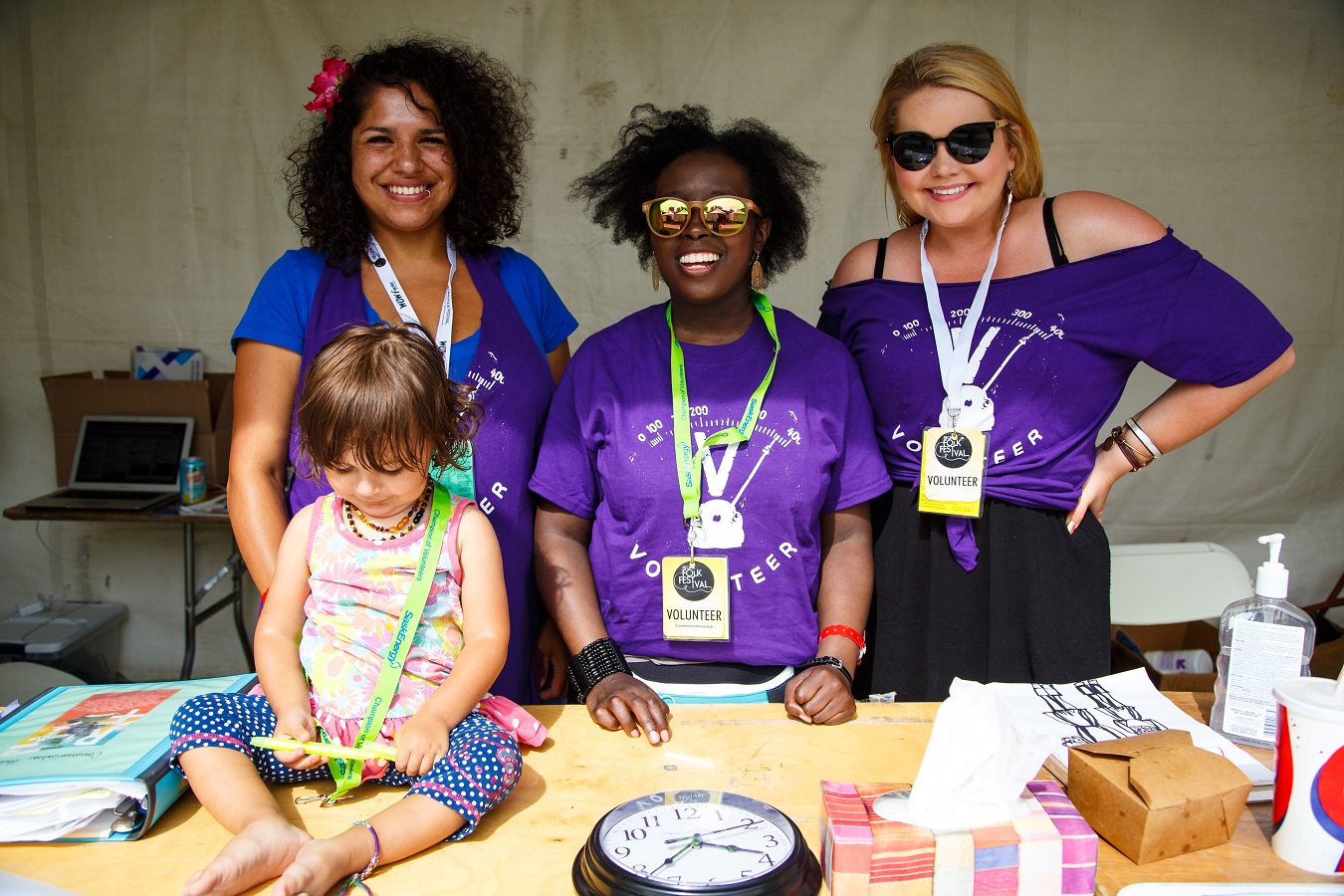 Three volunteers in purple shirts and a small child pose for a photo.