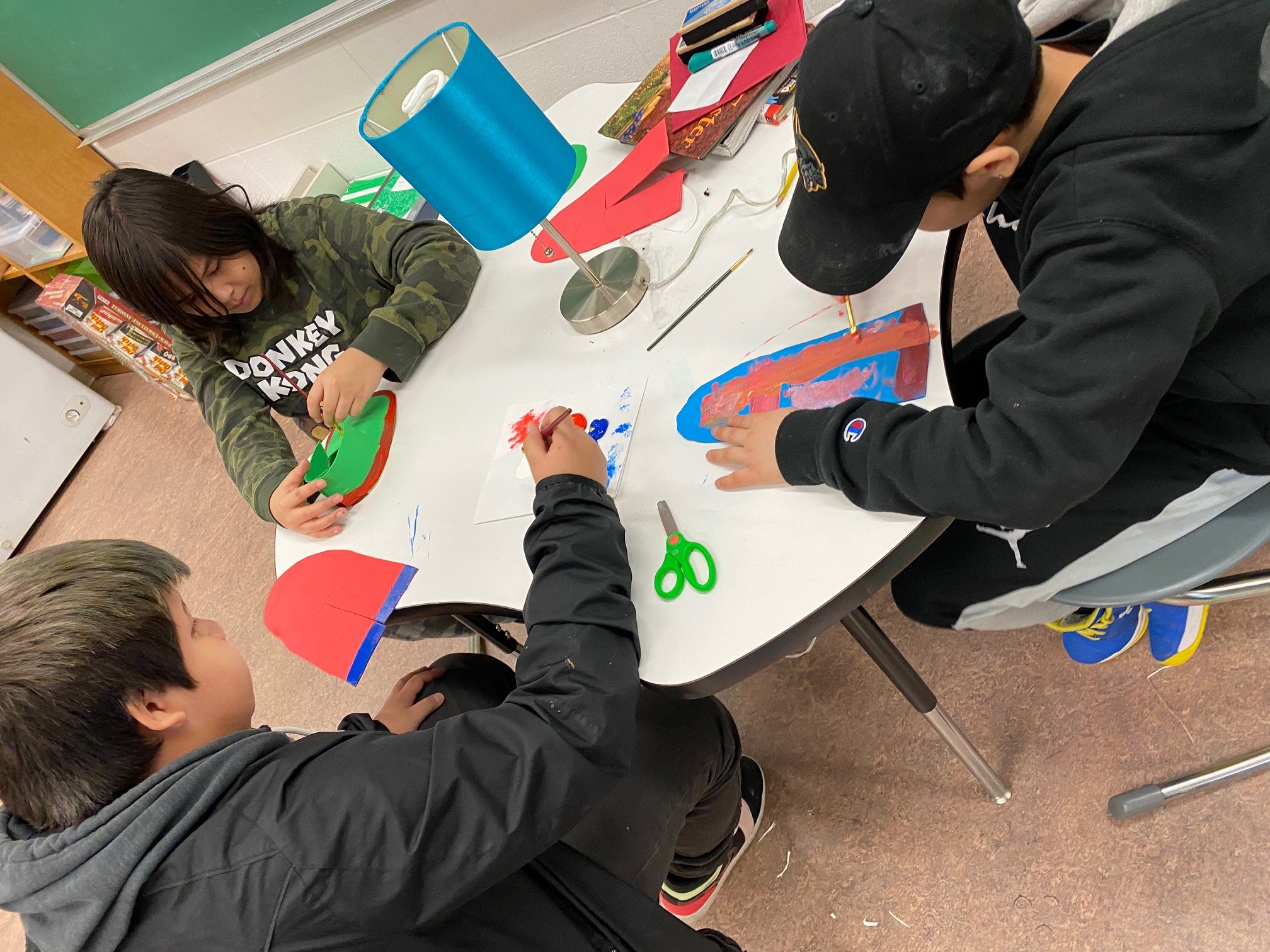 Three students create various kinds of artwork in a classroom.