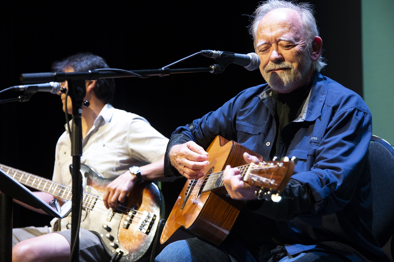Two musicians play guitars on stage.