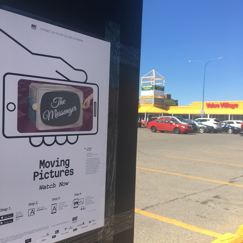A poster for the Moving Pictures project with a video still for the film "The Messenger" on a post in a Value Village parking lot.