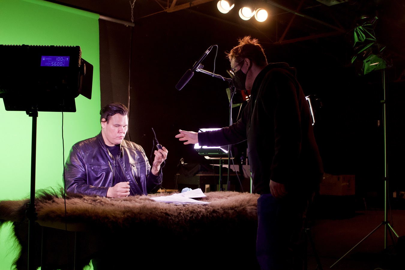 Lancelot Knight sits behind a news desk with Muskwa Lerat standing next to him