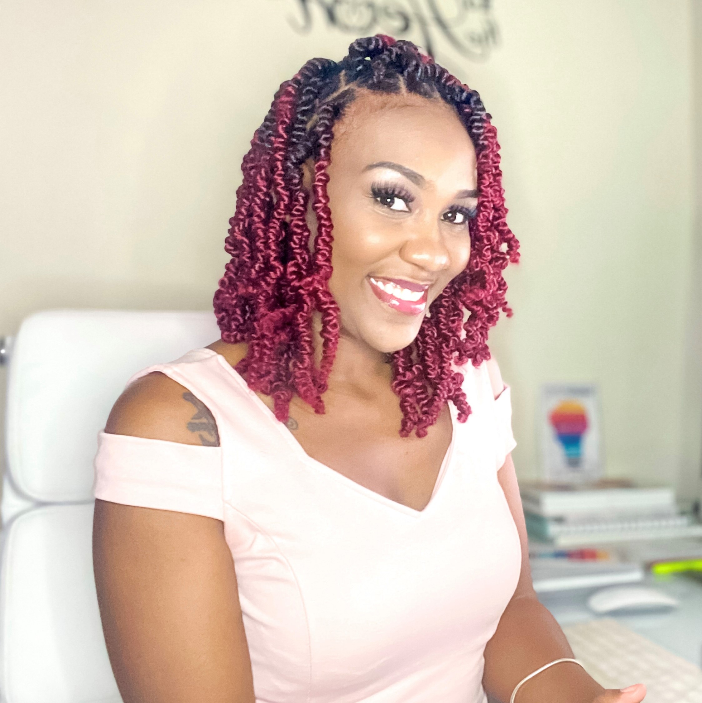 Shandean Reid, Communications Strategist - Black woman with black and red braids. She is wearing a light pink dress and smiling