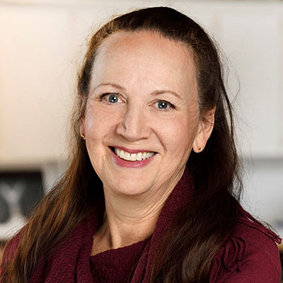 Carol Greyeyes, Policy and Planning Advisor - Indigenous woman with long hair smiling. She is wearing a red blouse.