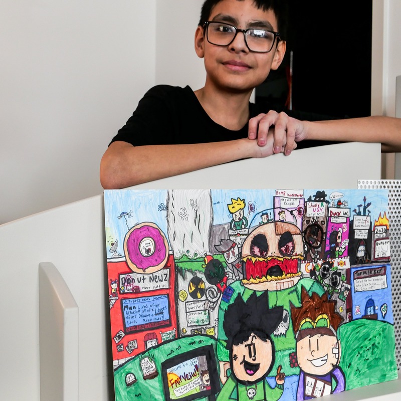Caine Head - Young boy wearing glasses and a black shirt with his artwork