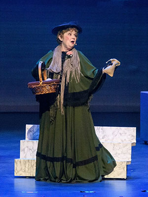 Marianne Woods in Mary Poppins. Woman on stage with blue background wearing a long green dress costume and she is performing.